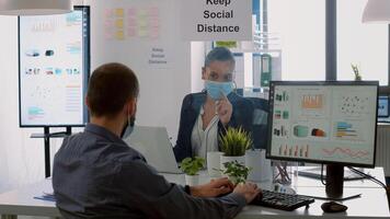 Business team with protection face masks working together in company office during corona virus global pandemic. Coworkers keeping social distancing while typing on computer checking reports photo