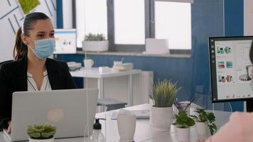 Freelancers wearing protective face masks working on computer in business office during global pandemic. Team sitting in new normal office respecting social distance to avoid infection with covid19 photo