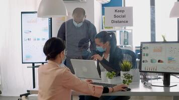 Team workers with protection face masks working in business office on computer during coronavirus lockdown. Coworkers keeping ing ing social distancing to avoid infection with virus disease photo