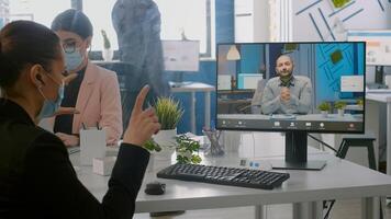 Freelancer wearing protective face mask during online videocall sitting at desk in startup company office. Coworkers working on computer during coronavirus global pandemic photo