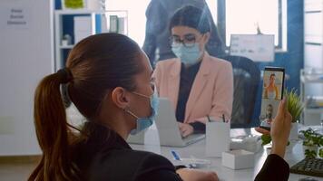 Back view of freelancer man with face mask talking on videocall meeting with remotely collegues using phone. Business woman working in new normal company office during covid19 pandemic photo