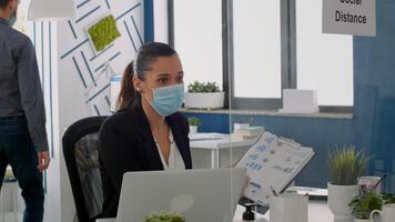 Freelancer wearing face mask to prevent infection with covid19 while showing financial graphs to her collegue. Business team keeping ing ing social distancing while working in company office photo