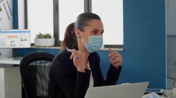 Businesswoman with medical face mask talking with her team about communication strategy sitting at desk. Business team keeping ing ing social distancing while working in new normal company office photo