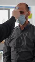 Freelancer man wearing protective mask against covid19 while checking temperature using medical thermometer to avoid infection with coronavirus. Company taking precautions during global pandemic photo