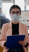 Front view of businesswoman wearing face mask while talking on online call meeting, the team working in background, keeping social distancing to avoid infection with covid19. Zoom conference teamwork photo
