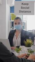 Freelancer with face mask working at financial graphics on pc sitting in business office. Coworkers talking in background about marketing mantain social distancing to prevent infection with covid19 photo