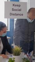 Business people with medical face masks sitting in new normal company office analysing financial project during covid19 pandemic. Coworkers keeping social distancing to avoid virus disease photo