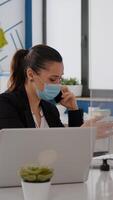 Woman with protective face mask working on laptop computer in company office checking statistics while talking on phone.Team workers respecting social distancing to avoid infection with covid19 virus photo