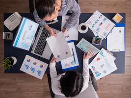 Top view of corporate business people doing good teamwork, working on financial stratey, looking at chart on paperwork, sitting at desk. Marketing team using tablet pc and laptop with documents. photo