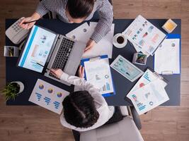 Top view of corporate business people doing good teamwork, working on financial stratey, looking at chart on paperwork, sitting at desk. Marketing team using tablet pc and laptop with documents. photo