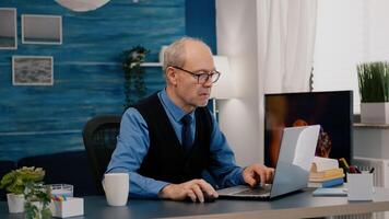 enfocado antiguo empresario comprobación gráficos escritura en ordenador portátil trabajando desde hogar Bebiendo café. retirado empleado utilizando moderno tecnología leyendo mecanografía, buscando mientras mayor esposa sentado en sofá foto