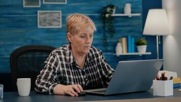Senior mature older woman watching business training, online webinar on laptop computer remote working, reading, analysing statistics from home. Old retired businesswoman typing, writing project photo