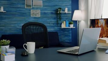 Pretty simple modern decor of cozy apartment with no people in it and television in background. Empty workspace of freelancer worker with laptop computer on desk and cup of coffee. photo