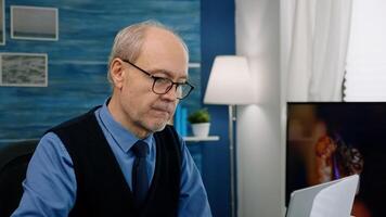 Close up of senior man writing at laptop working from home analysing financial project. Elegant retired employee with eyeglasses using modern technology reading typing on computer photo