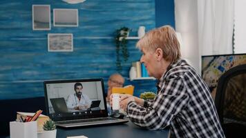 Remote doctor using webcam prescribing medicine to sick aged woman sitting in living room via internet. Patient talks with therapist by videoconference call application, holding pills flask photo