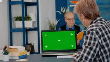Elderly person reading on green screen, mock up, chroma key display of laptop, writing on notebook working from home. Senior woman watching at pc with isolated desktop, while man sitting on sofa photo