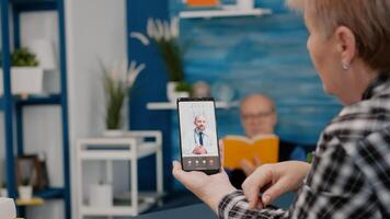 Middle aged woman talking at conference calling with remote doctor using smartphone. Remote physician using webcam prescribing medicine to sick aged patient sitting in living room via internet. photo