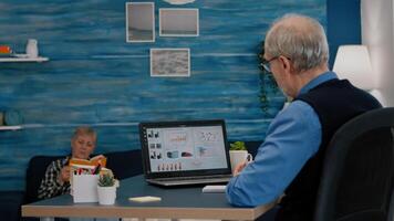 Middle aged senior older man e-learning online concept, watching business graphs, charts on laptop computer remote working, social distance learning, writing noteson notebook from home office. photo