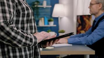 Close up of old woman employee texting, sending and reading messages on tablet during break standing in workplace. Businesswoman using modern technology network wireless overworking in midnight photo