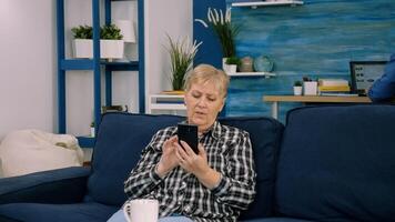 Overjoyed middle-aged woman sitting on couch in living room talking on call on smartphone gadget, happy excited senior female greeting speak on web using smartphone, technology concept photo
