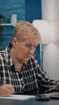 antiguo mujer empresario comprobación financiero proyecto de empresa mirando en ordenador portátil analizando anual Estadísticas datos, tomando notas en cuaderno sentado a escritorio en vivo habitación oficina trabajando desde hogar. foto