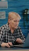 maduro caucásico dama trabajando en ordenador portátil a hogar lugar de trabajo, mecanografía en computadora Bebiendo café. experimentado gerente haciendo financiero proyecto durante yo aislamiento mientras marido leyendo un libro en antecedentes foto
