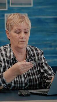 mayor mujer haciendo en línea pago utilizando crédito tarjeta en ordenador portátil trabajando desde hogar. retirado antiguo persona compras en línea, pago facturas, haciendo comercio electrónico actas utilizando moderno tecnología vía Internet foto