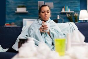 Woman with flu sitting at home drinking hot tea feeling sick. Person with temperature taking medicine for health virus infection, adult with disease pain headache photo