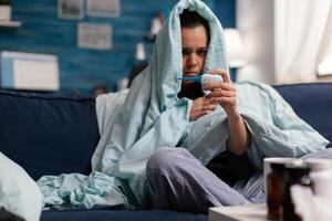 Caucasian woman measuring temperature ill at home with a thermometer. Person feeling sick cold unwell, checking fever and symptoms of disease flu infection. Resting adult with headache photo
