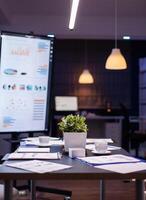Empty business company office meeting room with nobody in it having presentation monitor with corporate statistics. On conference table standing financial graphs documents photo