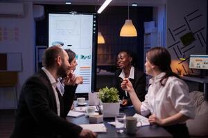 Executive manager woman explaining management statistics working at company strategy overtime in office meeting room. Diverse multi-ethnic businesspeople teamwork brainstorming ideas in evening photo