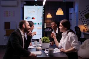 Executive manager woman explaining management statistics working at company strategy overtime in office meeting room. Diverse multi-ethnic businesspeople teamwork brainstorming ideas in evening photo