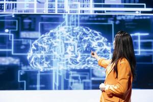 IT technician speaking at tech event, explaining impact of AI technology using AR visualization. Woman presenting risks and threats associated with AI, pointing towards augmented reality hologram photo