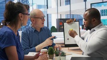 Insurance broker explaining financial plans to senior couple in a modern office, receiving expert advice on retirement plans. Discussing investment strategy, pension options and savings. Camera B. photo