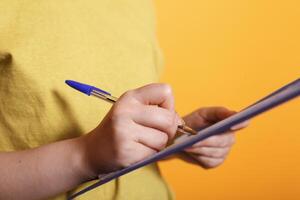 Close-up view of a Caucasian female hand writing on a clipboard with a pen. Woman filling out paperwork for freelance work, signing documents and making notes on a notepad. photo