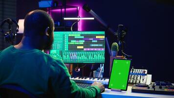 Songwriter composer mixing and mastering tracks next to green screen, operating on digital audio pc interface to add sound effects on new recordings. Technician in home studio. Camera B. photo