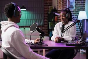 Online show host speaking with smiling african american guest during live broadcast for streaming service website. Internet influencer using professional devices to record podcast interview photo
