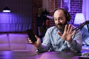 Portrait of tech vlogger listing top 5 best smartphones on the market in rgb lights home studio. Entertaining content creator filming technology listicle for interested audience photo