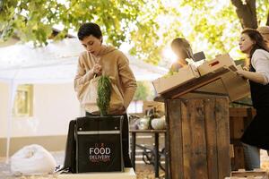 Female courier placing a package of locally grown veggies in thermal backpack, taking orders from farmers market. Young woman delivering freshly harvested healthy produce from local merchants. photo