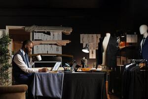 Relaxed couturier enjoying cup of coffee while sketching upcoming creative custom made sartorial collection. Skilled tailor in atelier studio workshop creating stylish garments photo