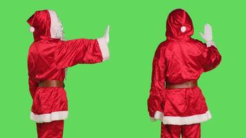 Santa character show palm as no, expressing stop symbol on camera with greenscreen backdrop. Model dressed like saint nick in red costume showing refusal gesture, holiday season concept. photo