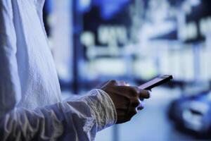 Man having fun walking around city at night, scrolling on online shopping platform using mobile phone, close up. Citizen using smartphone while strolling on empty streets blurry background photo