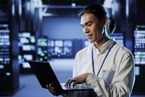 Qualified engineer in data center using laptop to prevent system overload during peak traffic periods. Diligent worker in server room ensuring there is enough network bandwidth for smooth operations photo