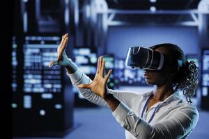 Tech support in data center uses virtual reality to prevent system overload. BIPOC VR technology user in server room ensuring enough network bandwidth for smooth operations photo