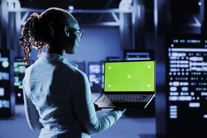 Computer operator builds firewall systems using green screen device in server room housing advanced infrastructure. Developer runs code on chrome key tablet to upgrade data center rigs photo