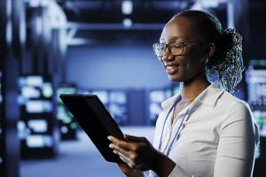Smiling woman between server hub rows providing processing resources for businesses worldwide. Happy admin fixing data center mainframes tasked with managing massive databases photo