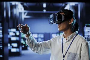Qualified programmer in data center uses virtual reality to prevent system overload. Specialist with VR goggles in server hub ensuring enough network bandwidth for smooth operations photo