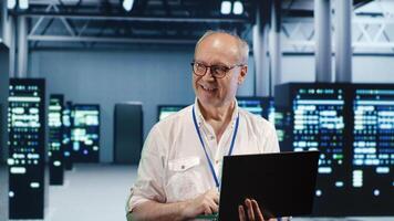 Elderly engineer expertly managing data while navigating in industrial server farm. Senior technician ensuring perfect cybersecurity protection, optimizing systems photo