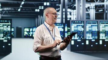 Meticulous IT professional navigating network of rackmounts in industrial server hub. Worker with laptop ensuring faultless operations, doing optimizations and maintenance in data center photo