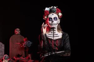 Woman at Day of the Dead event to remember the deceased, celebrating their memory, grave site background. Lady wearing skull face paint for mexican holiday of remembrance for those who have passed photo